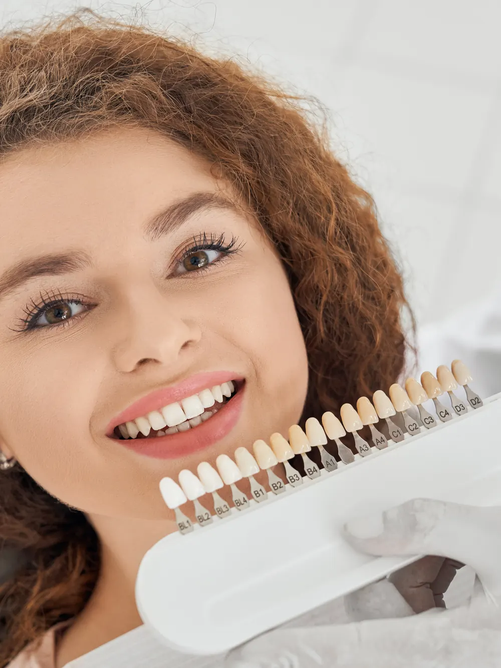 Ragazza sorridente dal professionista mentre sceglie con la scala colori la tonalità di bianco dei denti
